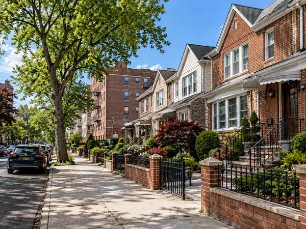 Attached houses on a tree-lined Queens-style street (illustrative image)